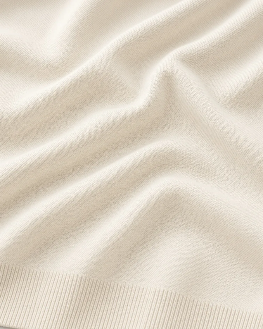 Malha do suéter Liso off-white de perto, em drapeado sobre fundo claro.