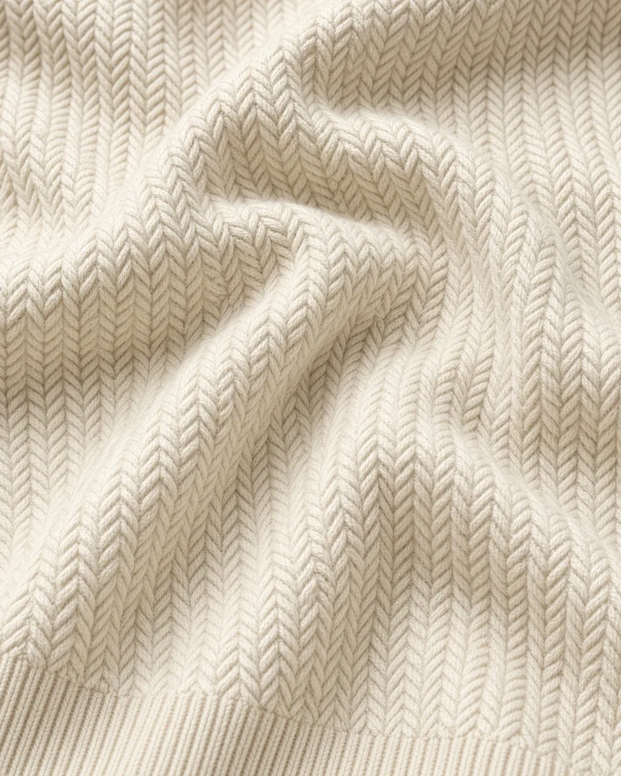 Malha do suéter Origami off-white de perto, em drapeado sobre fundo claro.